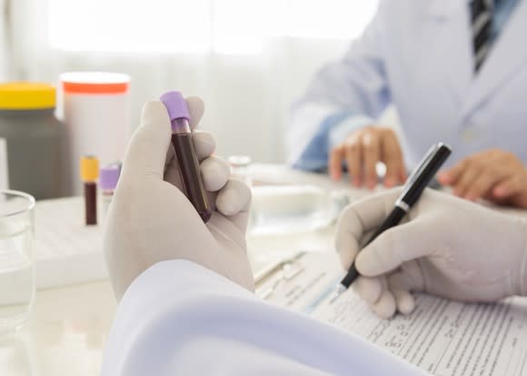 A pharmaceutical lab researcher holding a vial of blood and making notes.