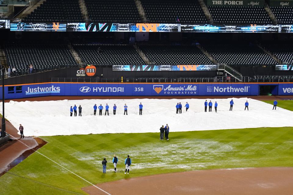 Officials stand on the field as members of the grounds crew watch during the rain delay of a baseball game between the New York Mets and the Miami Marlins early Friday, Sept. 29, 2023, in New York. (AP Photo/Frank Franklin II)