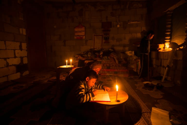 A Palestinian woman helps her son study, by candlelight, at their makeshift home in the Khan Yunis refugee camp in the southern Gaza Strip on April 19, 2017