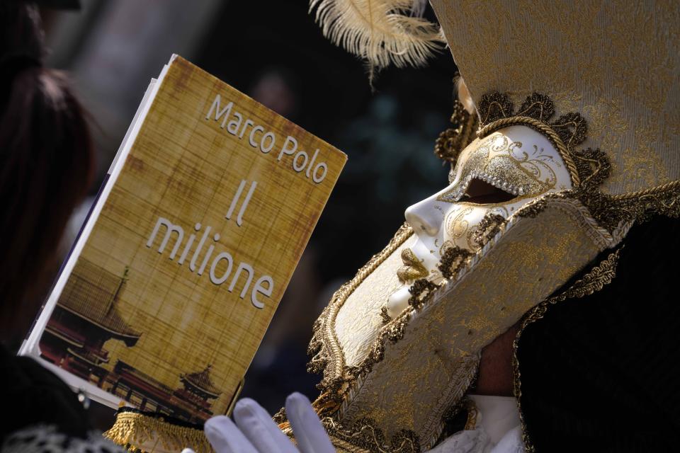 A man wears a mask and holds the replica a the book 'The Million" a report of Marco Polo's travels in Asia, during the Carnival in Venice, Italy, Sunday Jan. 28, 2024. Venice is marking the 700th anniversary of the death of Marco Polo with a yearlong series of commemorations, starting with the opening of Carnival season honoring one of the lagoon city's most illustrious native sons. (AP Photo/Luca Bruno)