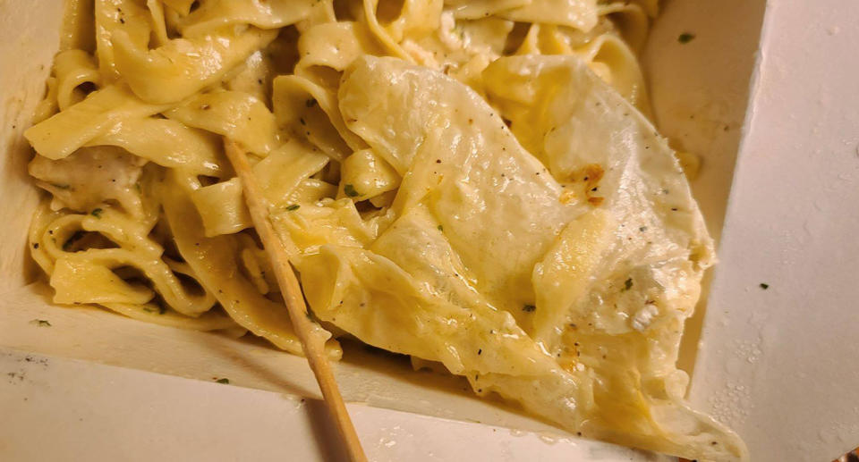 A disposable glove is covered in sauce on top of the pasta dish from The Cheesecake Factory.