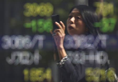 FILE PHOTO - A woman using a smartphone is reflected on a stock quotation board outside a brokerage in Tokyo, Japan, September 29, 2015. REUTERS/Issei Kato
