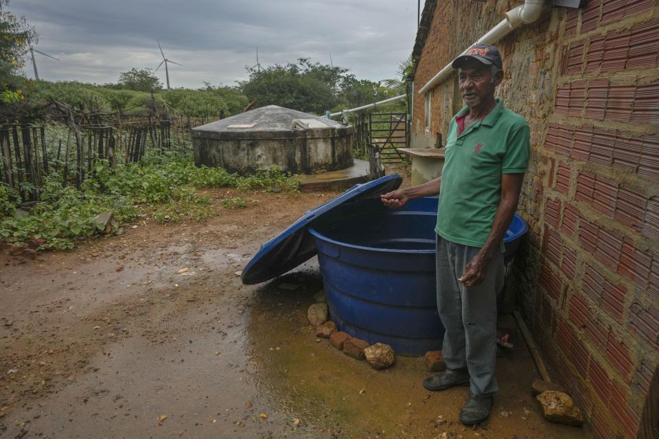 Joao de Souza Silva stands at his home with wind turbines visible in the distance in Sumidouro, Piaui state, Brazil, Wednesday, March 13, 2024. (AP Photo/Andre Penner)