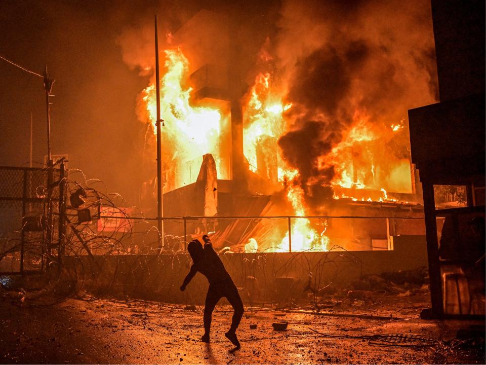 A Lebanese protestor hurls stones at burning building just outside the US Embassy during a protest in solidarity with the people of Gaza to condemn a strike against a hospital in Gaza Strip killing more than 500 people.
