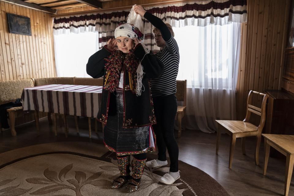 A neighbor helps Dr. Viktoria Mahnych to wear a Hutsul's traditional colorful clothes preparing to attend the Orthodox Christmas celebration in Iltsi village, Ivano-Frankivsk region of Western Ukraine, Thursday, Jan. 7, 2021. Ukraine is struggling to contain the coronavirus pandemic that has inundated its overburdened medical system, as Dr. Viktoria Mahnych goes door to door providing much needed help to patients.(AP Photo/Evgeniy Maloletka)