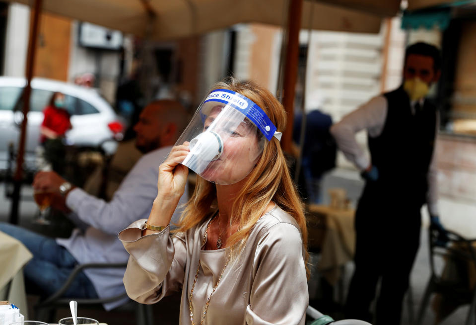 A woman wearing a face shield sips a coffee in a cafe in Rome.