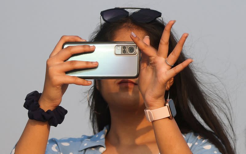 FILE PHOTO: A woman uses a smartphone on a beach in Mumbai