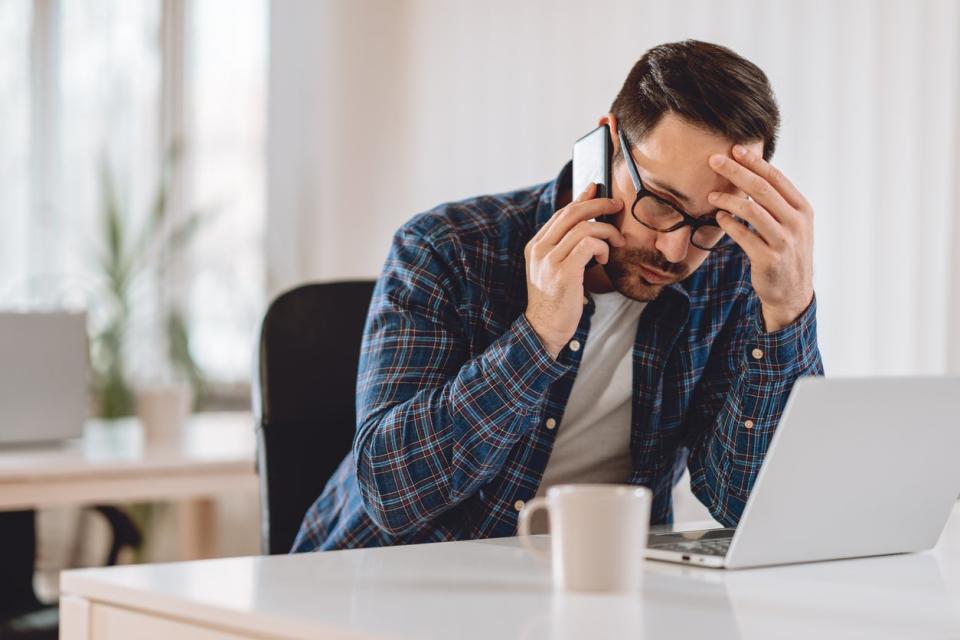 An impatient tenant sits at his desk on his cell phone waiting to get through to someone. 