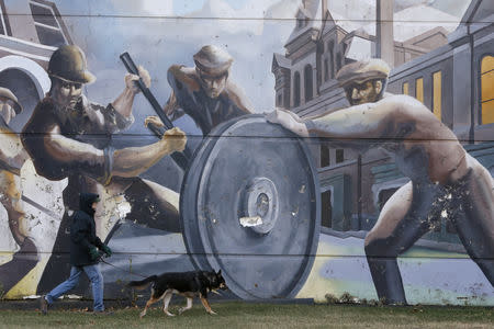 A man walks his dog past a mural depicting factory workers in the historic Pullman neighborhood in Chicago November 20, 2014. REUTERS/Andrew Nelles