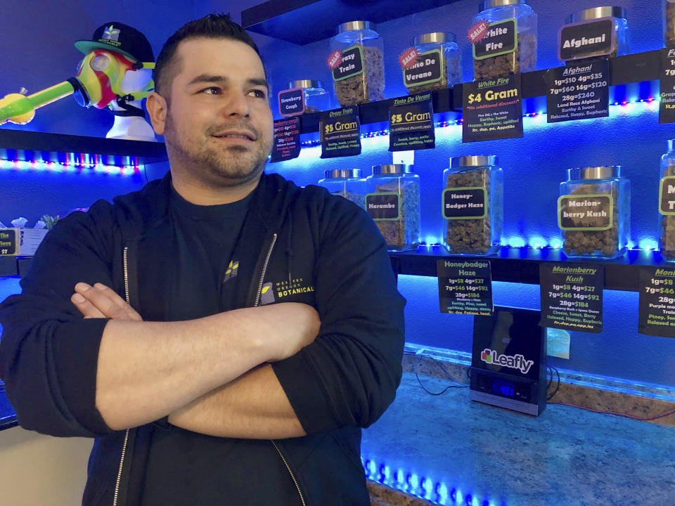 ADVANCE FOR PUBLICATION ON TUESDAY, JUNE 11, AND THEREAFTER - In this April 8, 2019, photo, Roberto Gonzalez, the general manager of Western Oregon Dispensary in Sherwood, Ore., poses for a photo in front of jars of medical marijuana. The dispensary is one of two medical-only marijuana dispensaries left in Oregon. An Associated Press analysis has found existing medical marijuana programs take a hit when states legalize cannabis for all adults. (AP Photo/Gillian Flaccus)