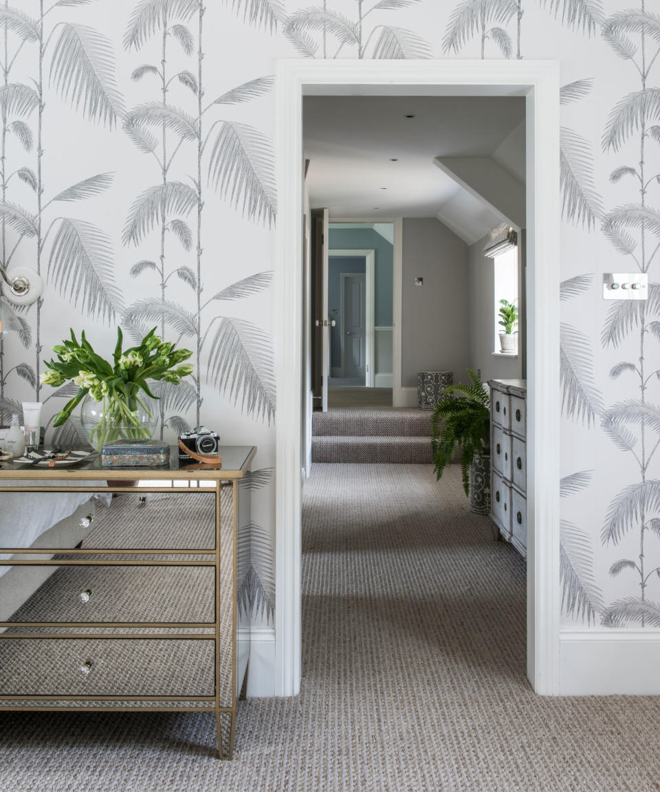 Bedroom with carpet, botanical leaf pattern light grey and white wallpaper and mirrored chest of drawers.  View along an upstairs corridor.