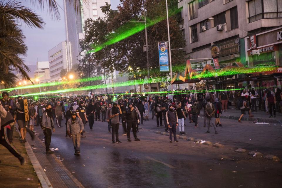 Anti-government protesters point green lasers at riot police in Santiago, Chile, Friday, Nov. 1, 2019. Chile has been facing days of unrest, triggered by a relatively minor increase in subway fares. The protests have shaken a nation noted for economic stability over the past decades, which has seen steadily declining poverty despite persistent high rates of inequality. (AP Photo/Rodrigo Abd)