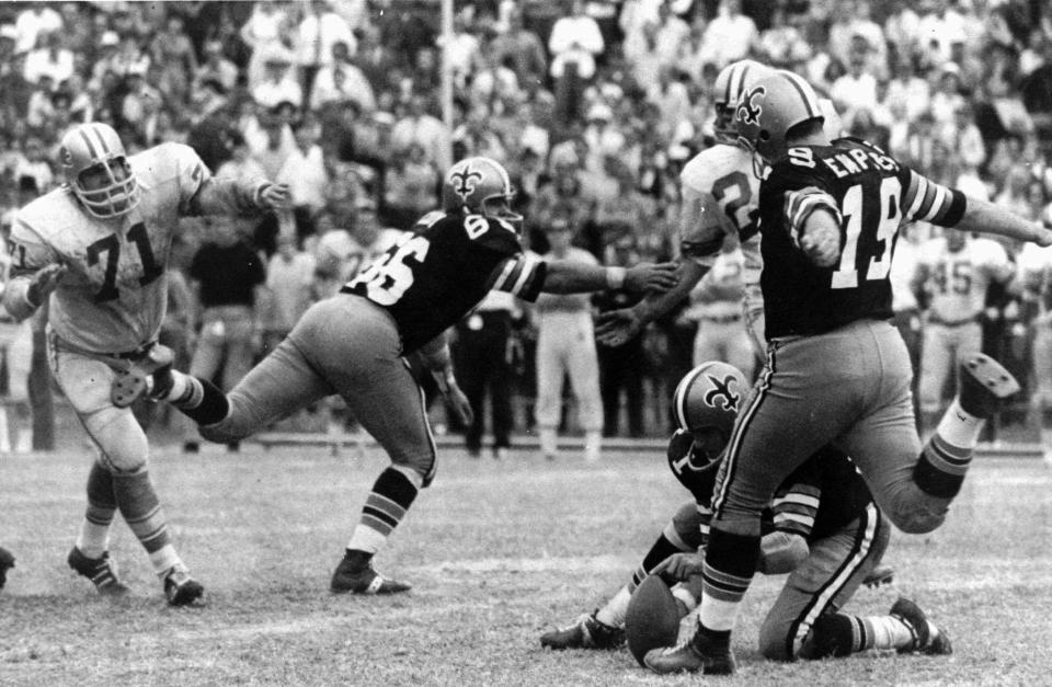 FILE - In this Nov. 8, 1970, file photo, New Orleans Saints' Tom Dempsey (19) moves up to kick a 63-yard field goal as teammate Joe Scarpati holds the ball and Detroit Lions' Alex Karras (71) rushes in while Saints' Bill Cody (66) blocks, in New Orleans. Dempsey, who played in the NFL despite being born without toes on his kicking foot and made a record 63-yard field goal, died late Saturday, April 4, 2020, in New Orleans while struggling with complications from the new coronavirus, his daughter said. He was 73 years old. (AP Photo/File)