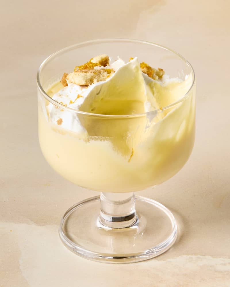 angled shot of a single dessert glass with orange creamsicle mousse, topped with whipped cream, crushed nilla wafers and orange shavings, and a bite taken out of it.