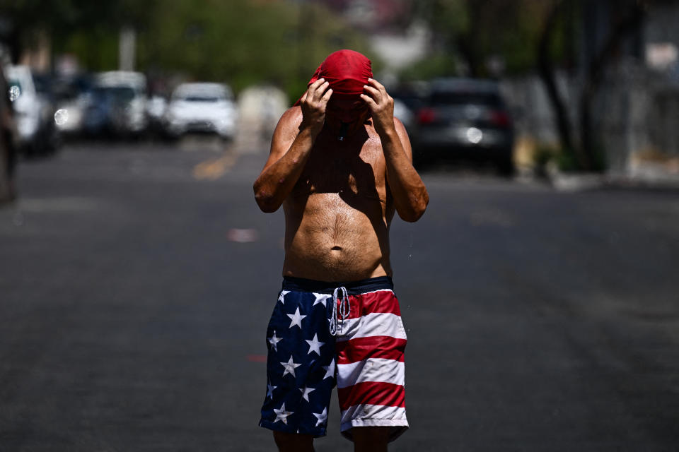 A shirtless person walks down the street in the sun.
