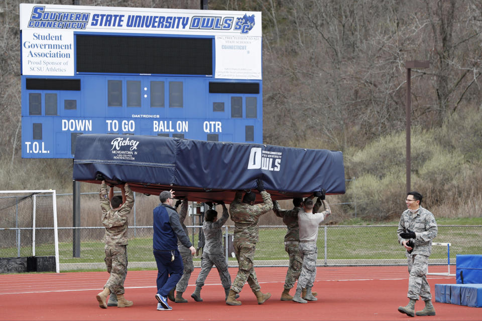 FILE- In this March 31, 2020 file photo, Connecticut Air and Army National Guard personnel move pole vault and high-jump mats to an outdoor field to make room inside Moore Field House for a temporary field hospital to be constructed to the current coronavirus crisis at Southern Connecticut State University in New Haven, Conn. Although New York City is the epicenter of the coronavirus outbreak, the virus has significantly impacted cities and towns in New Jersey and Connecticut. (AP Photo/Kathy Willens)
