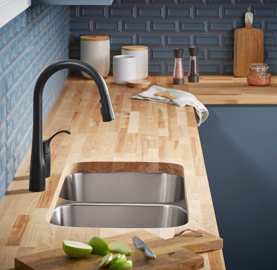 Modern kitchen with black faucet, stainless steel sink, wooden countertop, and various cooking accessories