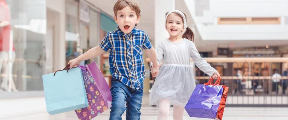 Group portrait of two cute adorable preschool children going shopping. Caucasian little girl and boy running in mall. Kids holding shopping bags.