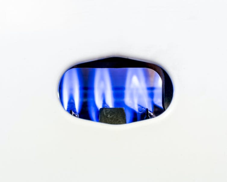 The blue pilot light inside a white gas boiler.