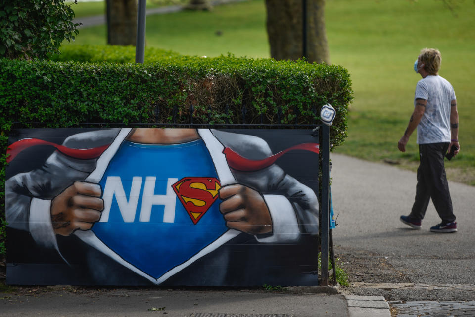 LONDON, ENGLAND  - APRIL 11: A man wearing a mask walks past an NHS graffiti sign at Hilly Fields, South London on April 11, 2020 in London, England. Public Easter events have been cancelled across the country, with the government urging the public to respect lockdown measures by celebrating the holiday in their homes. Over 1.5 million people across the world have been infected with the COVID-19 coronavirus, with over 7,000 fatalities recorded in the United Kingdom.   (Photo by Peter Summers/Getty Images)
