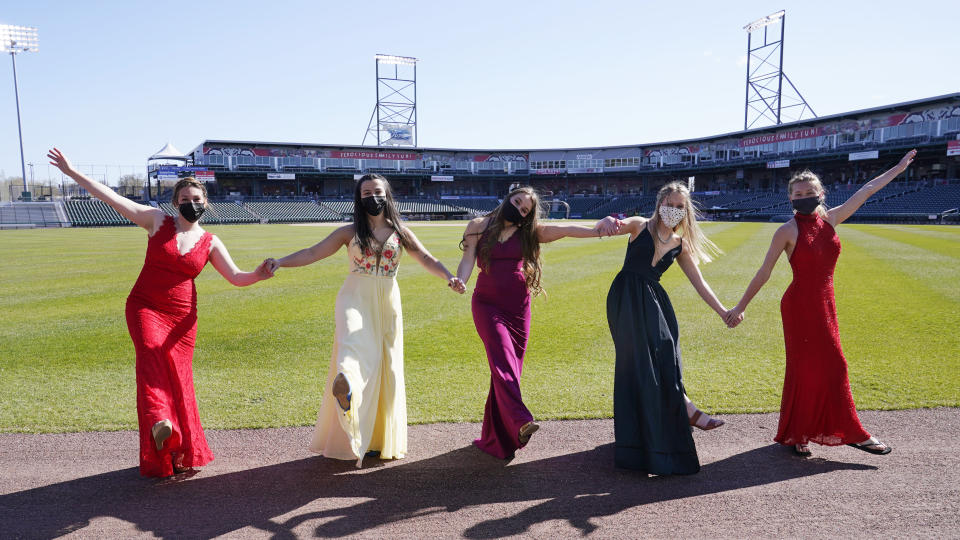 While wearing their prom gowns, students pose for a photograph in the outfield at the New Hampshire Fisher Cats minor league baseball stadium in Manchester, N.H., on Monday, April 26, 2021. After a year without proms, school districts across the country are debating whether they can safely hold an event that many seniors consider a capstone to their high school experience. The nearly 300 student senior class of Manchester's Central High School are waiting to get approval from the city's board of health so they can have their prom at the outdoor venue, due to COVID-19 concerns. (AP Photo/Charles Krupa)
