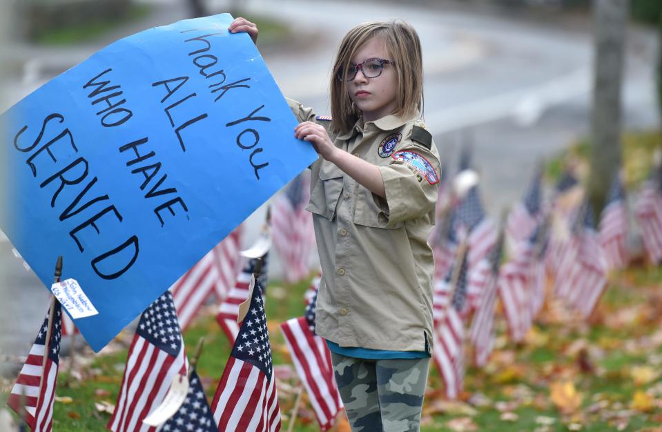 Nine-year-old Jaelyn Santos, a Centerville Pack 54 Cub Scout, stands in a lawn full of red, white and blue as she welcomes arriving veterans to a drive-through Veterans Day event hosted at St. Mary's Church in Barnstable.