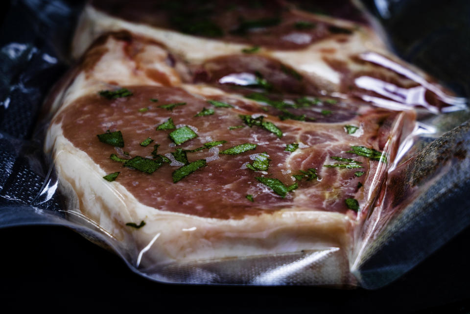 Raw steak in vacuum-sealed packaging with sprinkled herbs