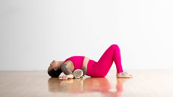 A person demonstrates a variation of Matsyasana (Fish Pose) in yoga, with a rolled blanket under her back