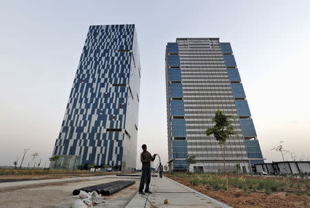 A worker folds the cable of a welding machine in front of two office buildings at the Gujarat International Finance Tec-City (GIFT) at Gandhinagar, in the western Indian state of Gujarat, April 10, 2015. REUTERS/Amit Dave