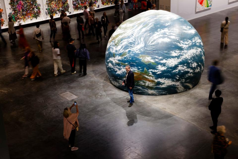 A giant inflatable balloon painted to resemble the Earth sits on a gallery floor surrounded by people and other art.