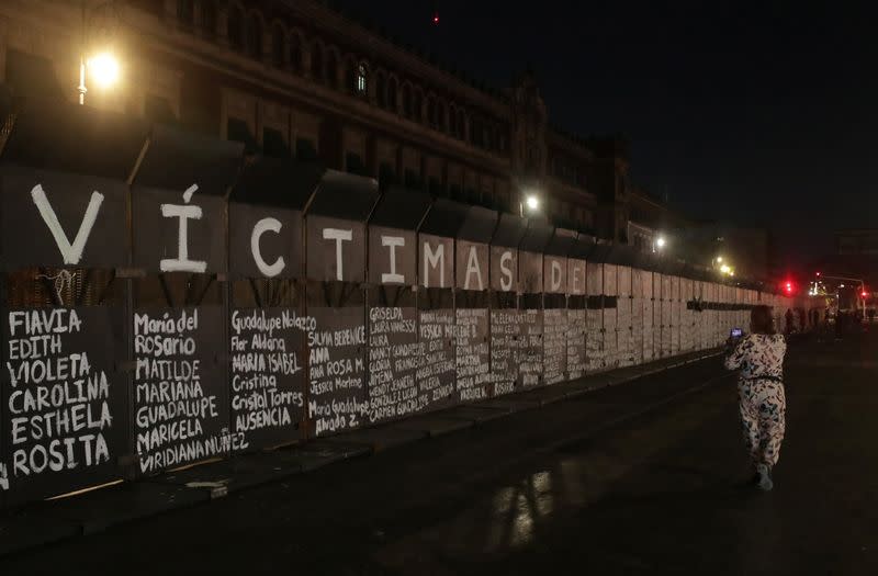 A visitor takes pictures with her mobile the names of victims of femicide in Mexico painted by women on fences placed outside the National Palace in Mexico City