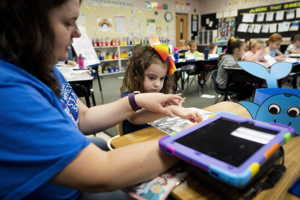 Vivien Henshall, a long-term substitute special education teacher, works with Scarlett Rasmussen separately as other classmates listen to instructions from their teacher at Parkside Elementary School Wednesday, May 17, 2023, in Grants Pass, Ore. Chelsea has fought for more than a year for her 8-year-old daughter, Scarlett, to attend full days at Parkside and says school employees told her the district lacked the staff to tend to Scarlett’s medical and educational needs, which the district denies. She was born with a genetic condition that causes her to have seizures and makes it hard for her to eat and digest food, requiring her to need a resident nurse at school. (AP Photo/Lindsey Wasson)