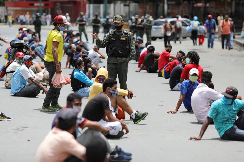 Foto del miércoles de un miembro de la Guardia nacional de Venezuela entre un grupo de personas sentadas bajo el sol por no cumplir con las normas de salud por la pandemia de coronavirus en una calle en Caracas