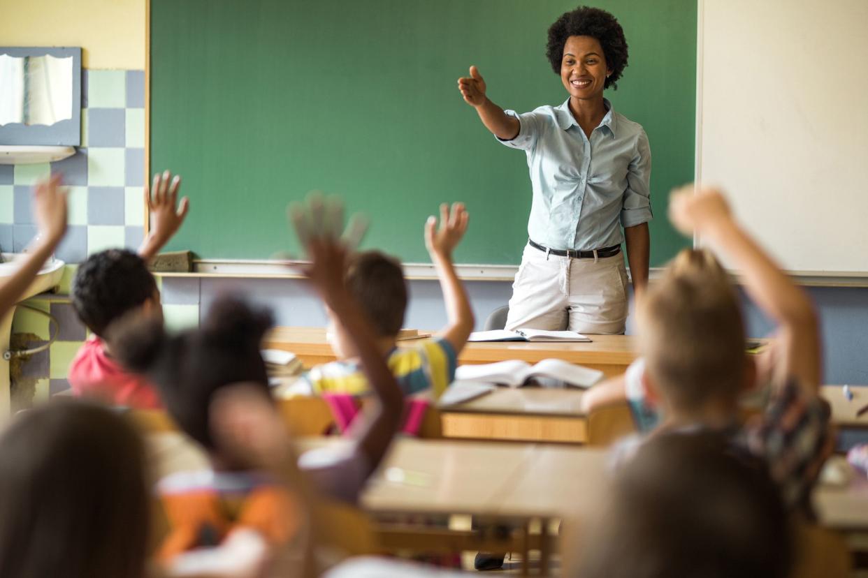 teacher standing in front of class with hands raised, about to call on student