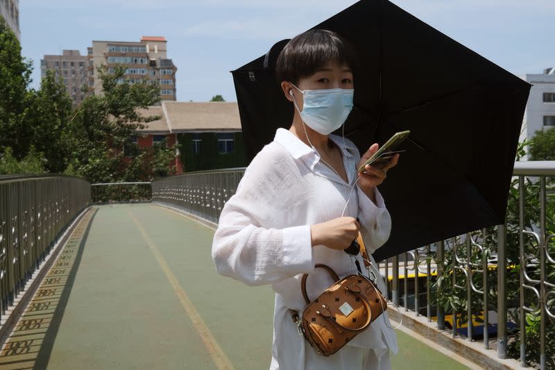 Woman wearing a face mask holds an umbrella as she walks on an overpass, following the outbreak of the coronavirus disease (COVID-19), in Beijing