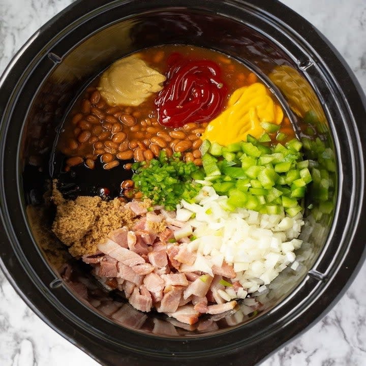 Beans, ham, ketchup, mustard, and onions in a slow cooker.