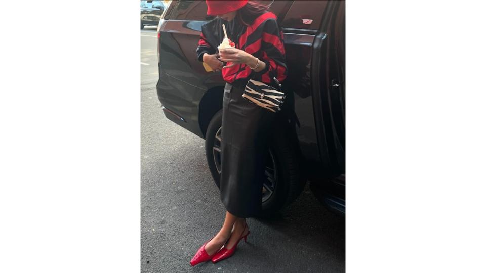 Dua Lipa poses next to a car in a leather midi skirt, red heels and a red and black jacket