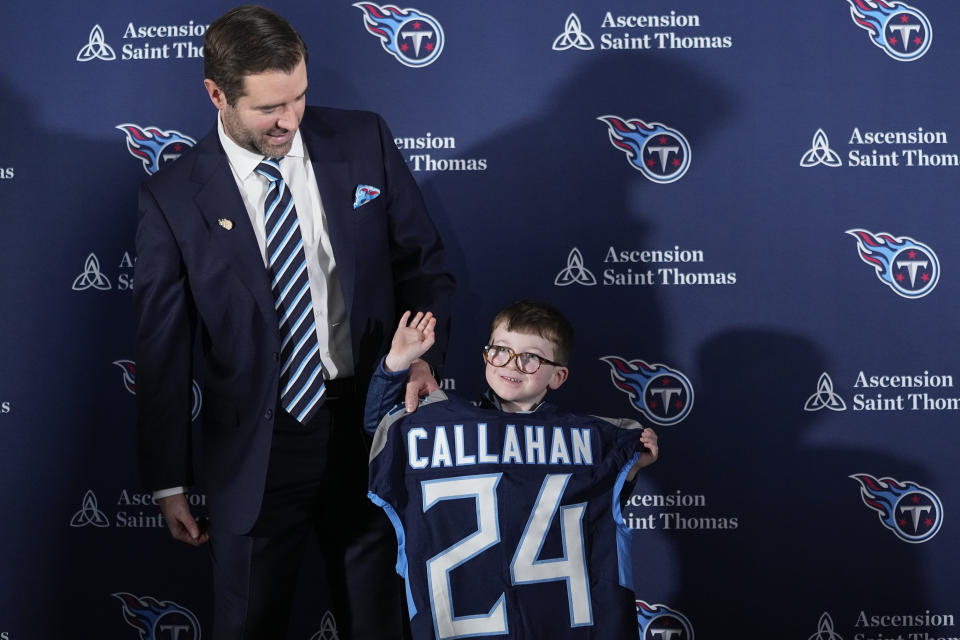 Ronan Callahan, right, son of Tennessee Titans new head football coach Brian Callahan, left, waves to photographers after an introductory news conference at the NFL team's training facility Thursday, Jan. 25, 2024, in Nashville, Tenn. (AP Photo/George Walker IV)