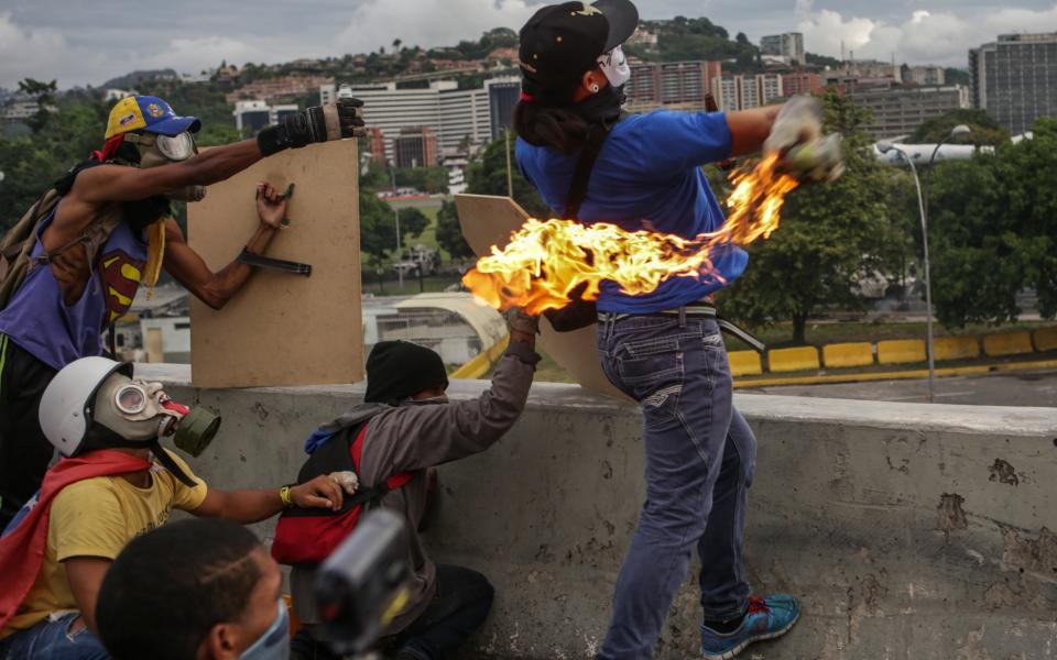 A masked demonstrator throws a Molotov cocktail during a protest organized by opponents of the Venezuelan government in Caracas - Credit: EFE via EPA