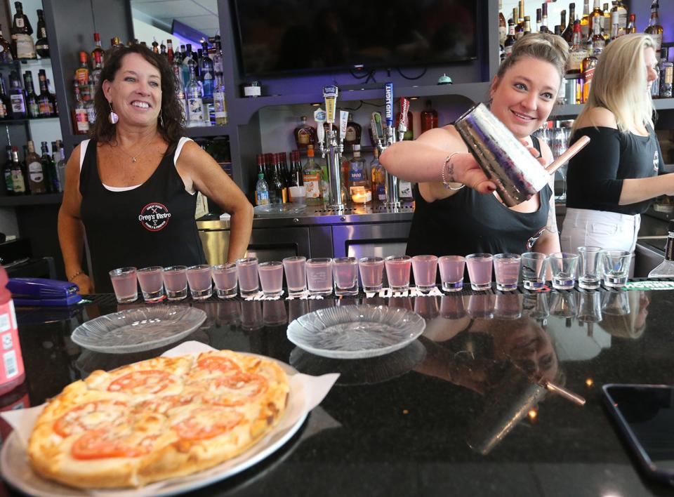 Greg's Bistro bartender Jennifer Morin carefully pours a number of shots to hand out to customers during the grand reopening of the Hampton eatery Wednesday, June 28, 2023.  She is seen with Christine Anzalone, left, and Reese Carson, right.
