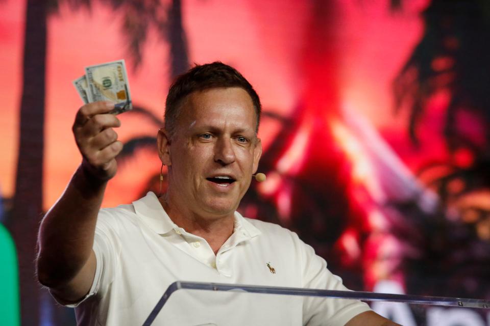 Peter Thiel, co-founder of PayPal, Palantir Technologies, and Founders Fund, holds hundred dollar bills as he speaks during the Bitcoin 2022 Conference at Miami Beach Convention Center on April 7, 2022 in Miami, Florida. 