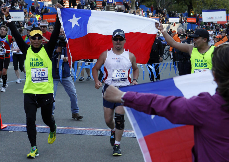 Chilean miner Edison Pena (C) crosses the finish line of the New York City Marathon, November 7, 2010. At far right is Pena' wife Angelica Alvarez holding a Chilean flag.  REUTERS/Mike Segar   (UNITED STATES - Tags: SPORT ATHLETICS)