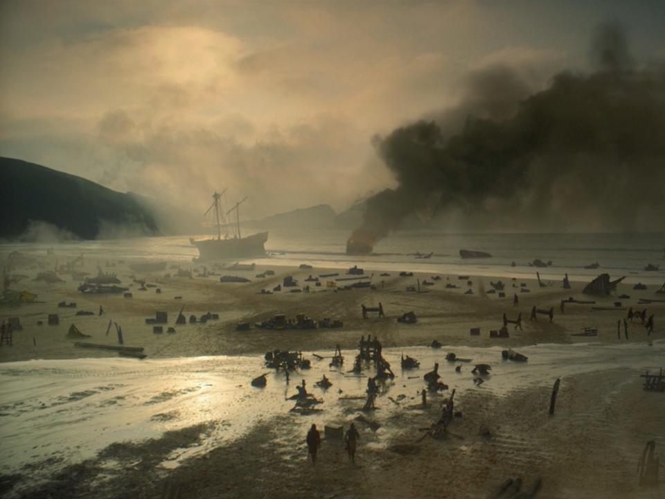 A scene from "House of the Dragon," showing a beach with the tide out covered in corpses and crabs, with a ship on fire in the distance.