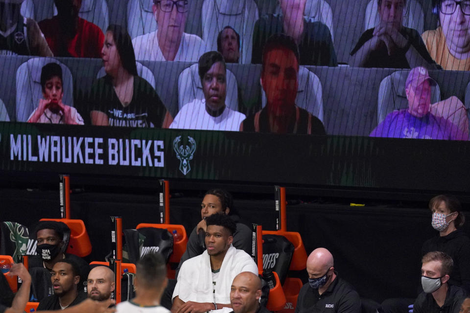 Milwaukee Bucks' Giannis Antetokounmpo (34), center bottom with towel, watches play as virtual fans, above, are shown during the second half of an NBA basketball conference semifinal playoff game against the Miami Heat on Monday, Aug. 31, 2020, in Lake Buena Vista, Fla. (AP Photo/Mark J. Terrill)