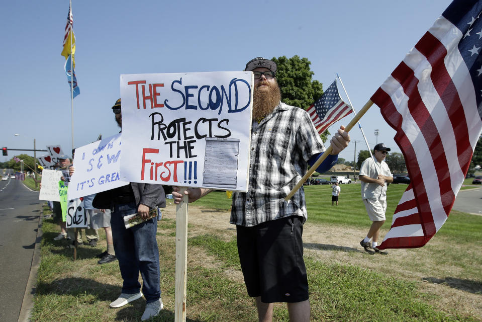 John Allen, of Worcester, Mass., center, holds a placard defending Second Amendment rights near the headquarters of gun manufacturer Smith & Wesson, Sunday, Aug. 26, 2018, in Springfield, Mass., along the planned route of a 50-mile march of protesters calling for gun law reforms. (AP Photo/Steven Senne)