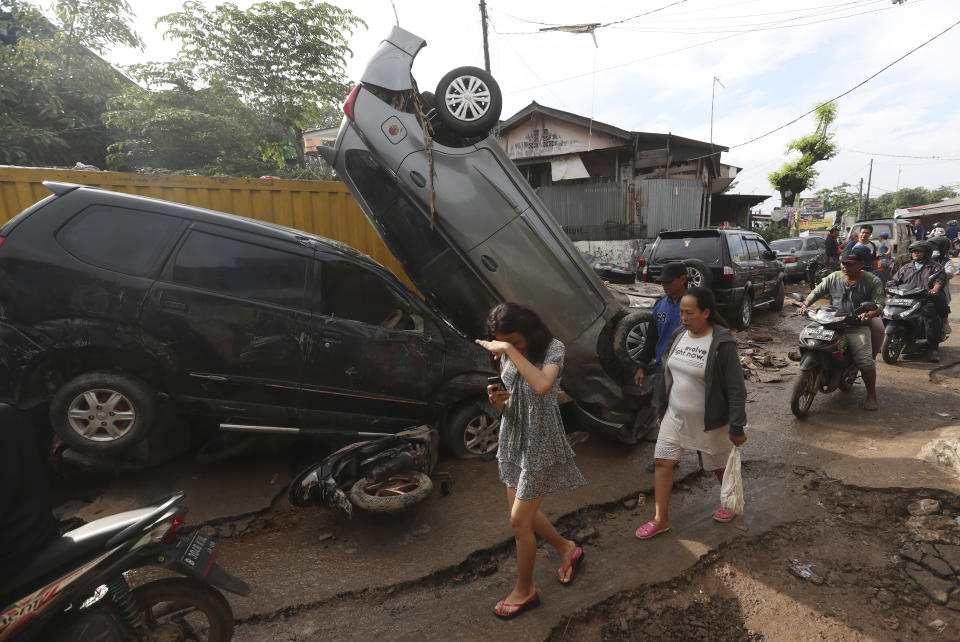 Residents walk near the wreckage of cars that were swept away by flood in Bekasi, West Java, Indonesia, Friday, Jan. 3, 2020.Severe flooding in greater Jakarta has killed scores of people and displaced tens of thousands others, the country's disaster management agency said. (AP Photo/Achmad Ibrahim)