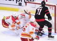 Calgary Flames goaltender David Rittich (33) gets a face full of snow from teammate Calgary Flames centre Dillon Dube (29) as the puck floats above him while Ottawa Senators centre Chris Tierney (71) looks on during third period NHL hockey action in Ottawa on Monday, March 1, 2021. (Sean Kilpatrick/The Canadian Press via AP)