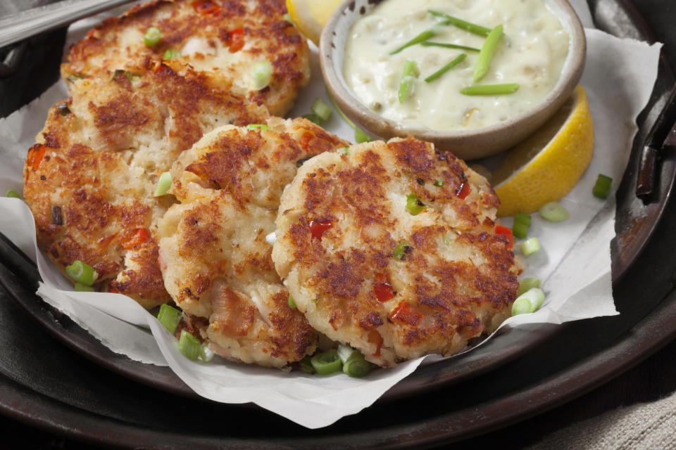 small discs of crab cakes layered on a plate with a side of sauce