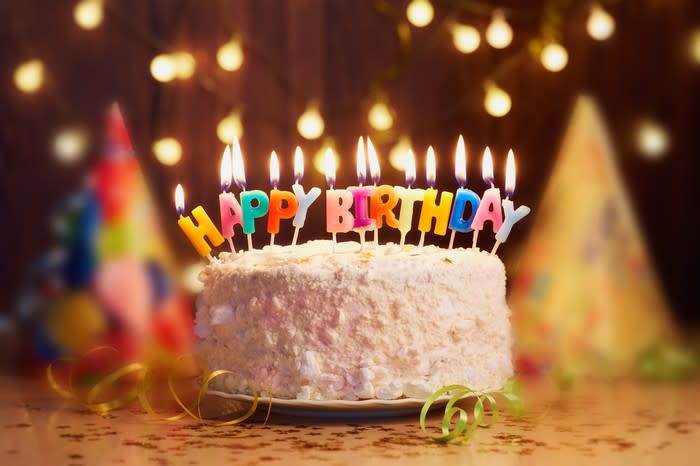 A birthday cake with lit candles that spell out, happy birthday.