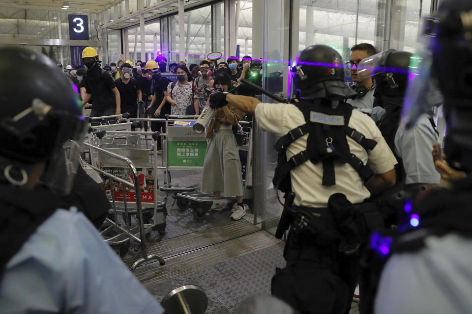 Policemen in riot gears face protesters at the main entrance of the airport during a demonstration in Hong Kong, Tuesday, Aug. 13, 2019. Chaos has broken out at Hong Kong's airport as riot police moved into the terminal to confront protesters who shut down operations at the busy transport hub for two straight days. (AP Photo/Kin Cheung)
